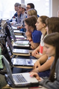Students listen to a lecture while taking notes on laptop computers.
